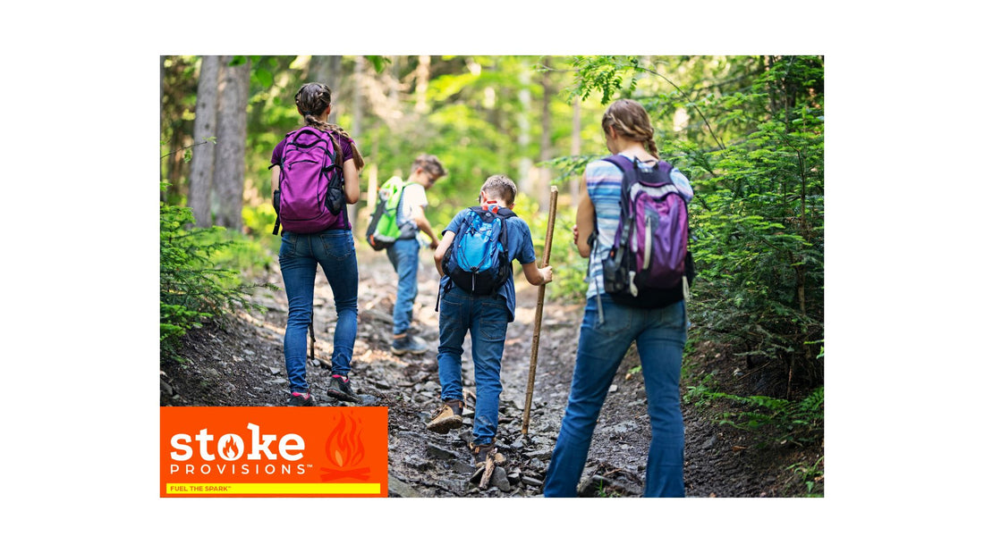 A diverse group of young adults hiking and enjoying a snack break with beef snack sticks in a lush, green outdoor setting under a clear sky.